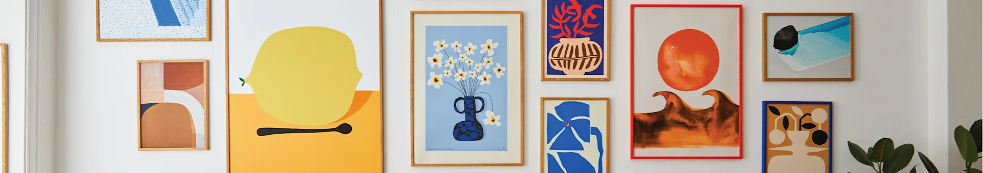 En gallerivæg med flere abstrakte kunstprint i forskellige farver og stilarter, herunder en gul citron, blomster i en vase og geometriske former.
