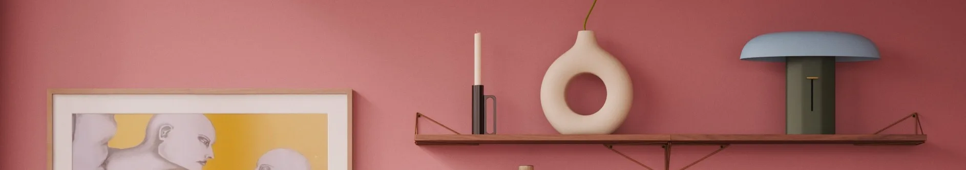 En pink væg, træhylde: hvidt lys, creme donutvase med grøn stilk, blå/grøn lampe. Indrammet kunstværk til venstre.