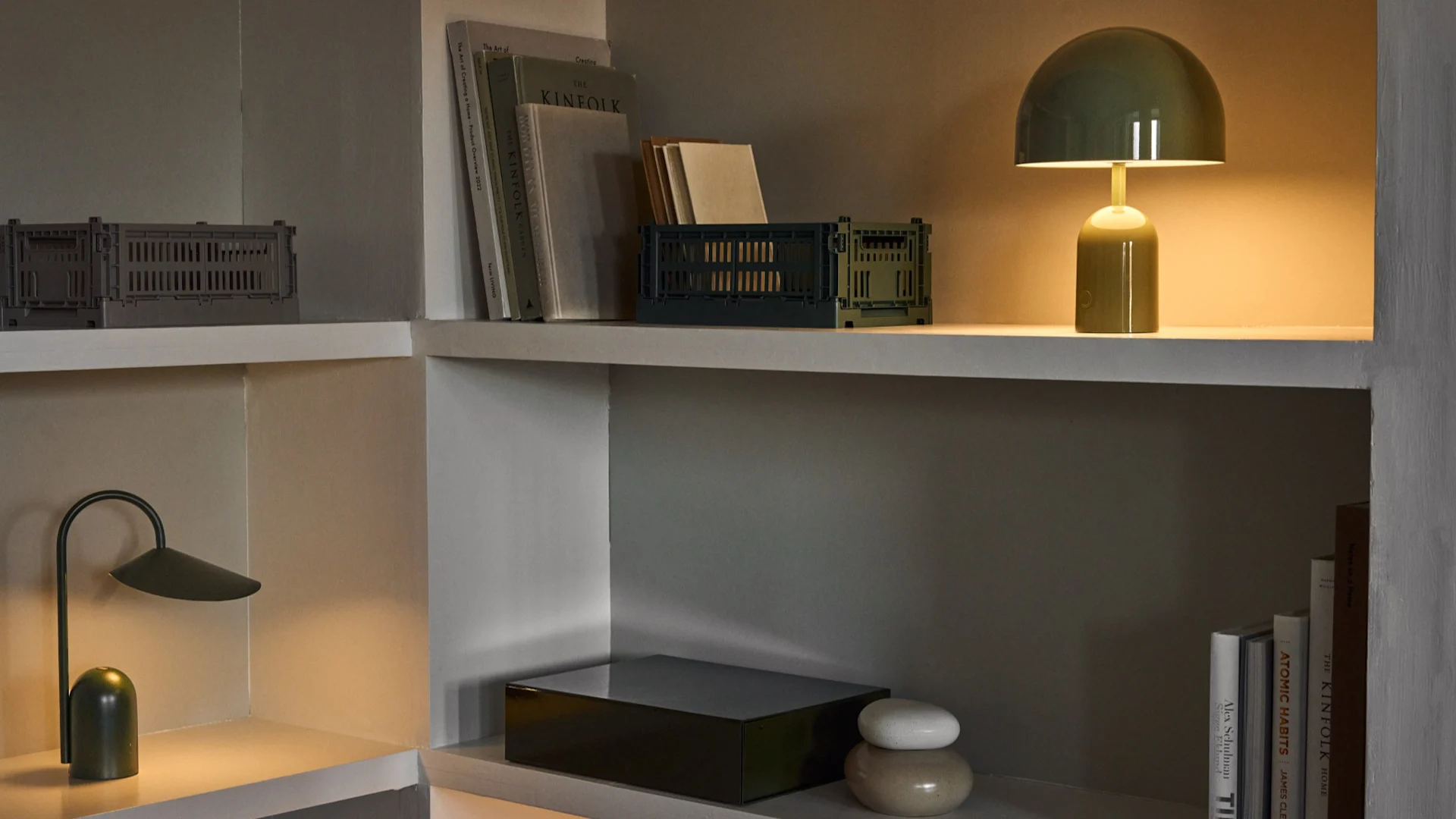 Hyldereol med grønne kasser, bøger, en grøn champignonlampe, en mørkegrøn bordlampe og keramiske dekorationer.