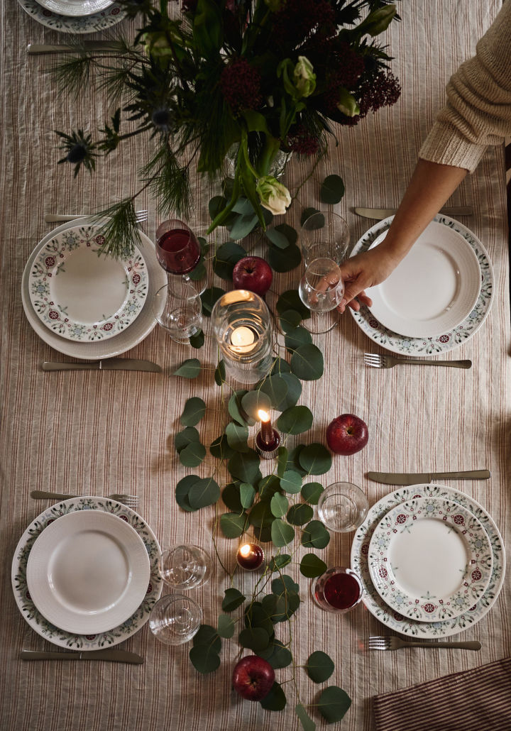 En enkel og elegant idé til juleborddækning fotograferet fra oven med grønne blade og røde æbler som dekoration. 