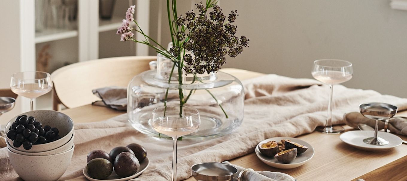 En romantisk borddækning med tallerkener og skåle fra By On sammen med elegante champagneglas fra Blomus.