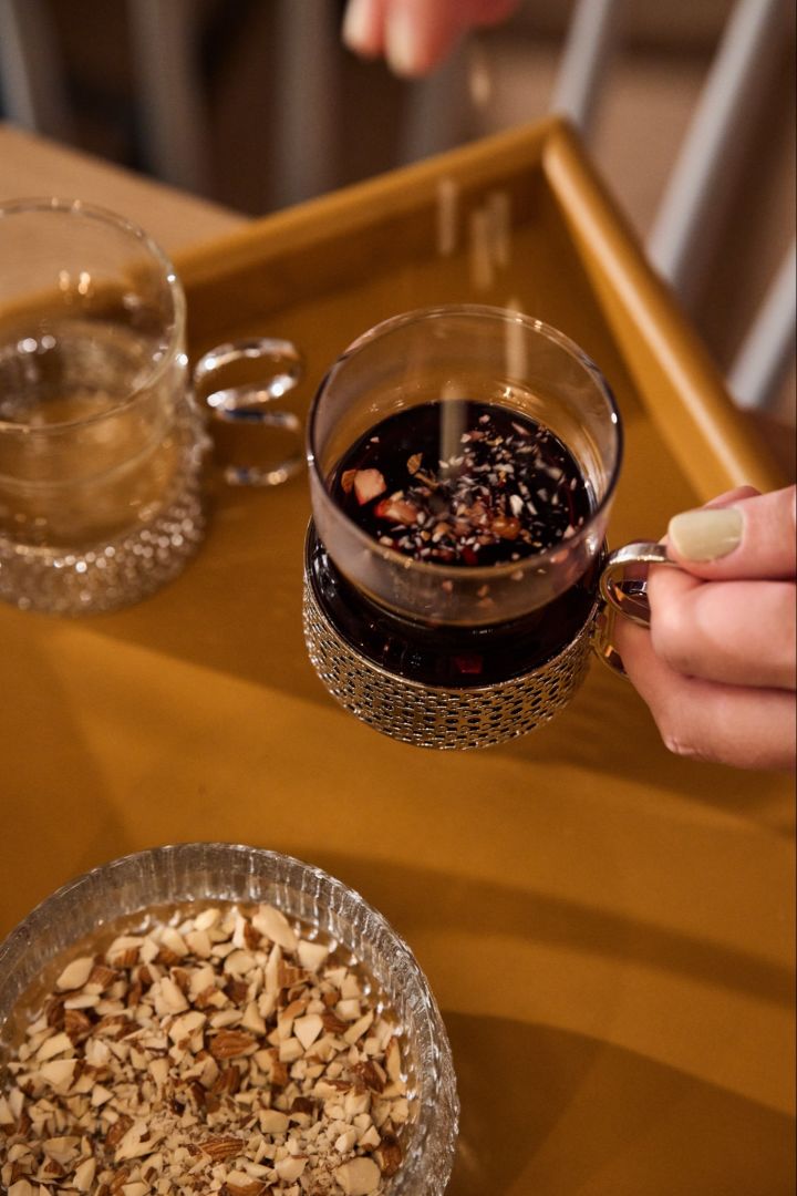 En hånd drysser mandler i et traditionelt glas gløgg på et nordisk julebord.