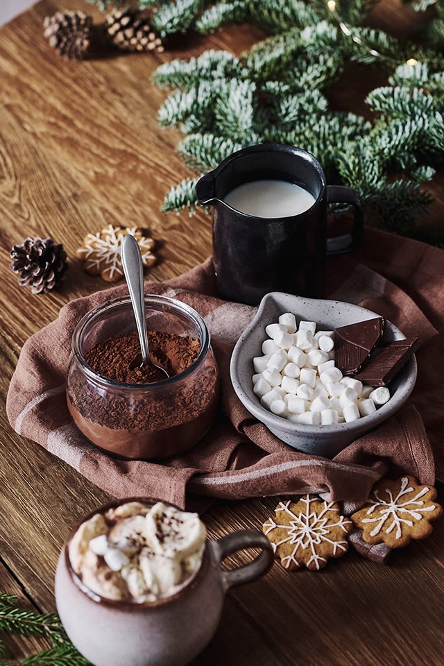 Adventshygge med varm chokolade og dens ingredienser som kakao, mælk og mini marshmallows står ved siden af i skåle. 