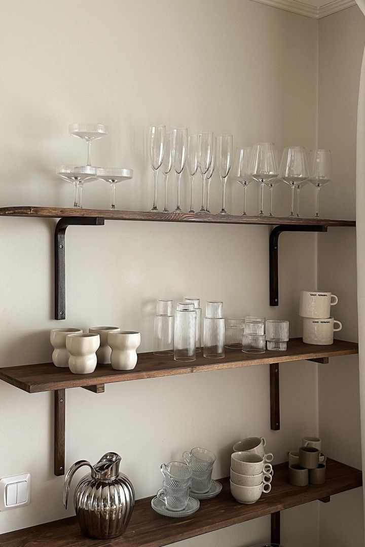 En hylde med glas og kopper i nærheden af kaffebaren er også en god idé. Her kan du se en hylde i tre etager med Limfjord-krus fra Broste Copenhagen, forskellige Ripple-glas fra ferm LIVING og Freckle-krus fra Scandi Living i den svenske influencer Joanna Aventos køkken.