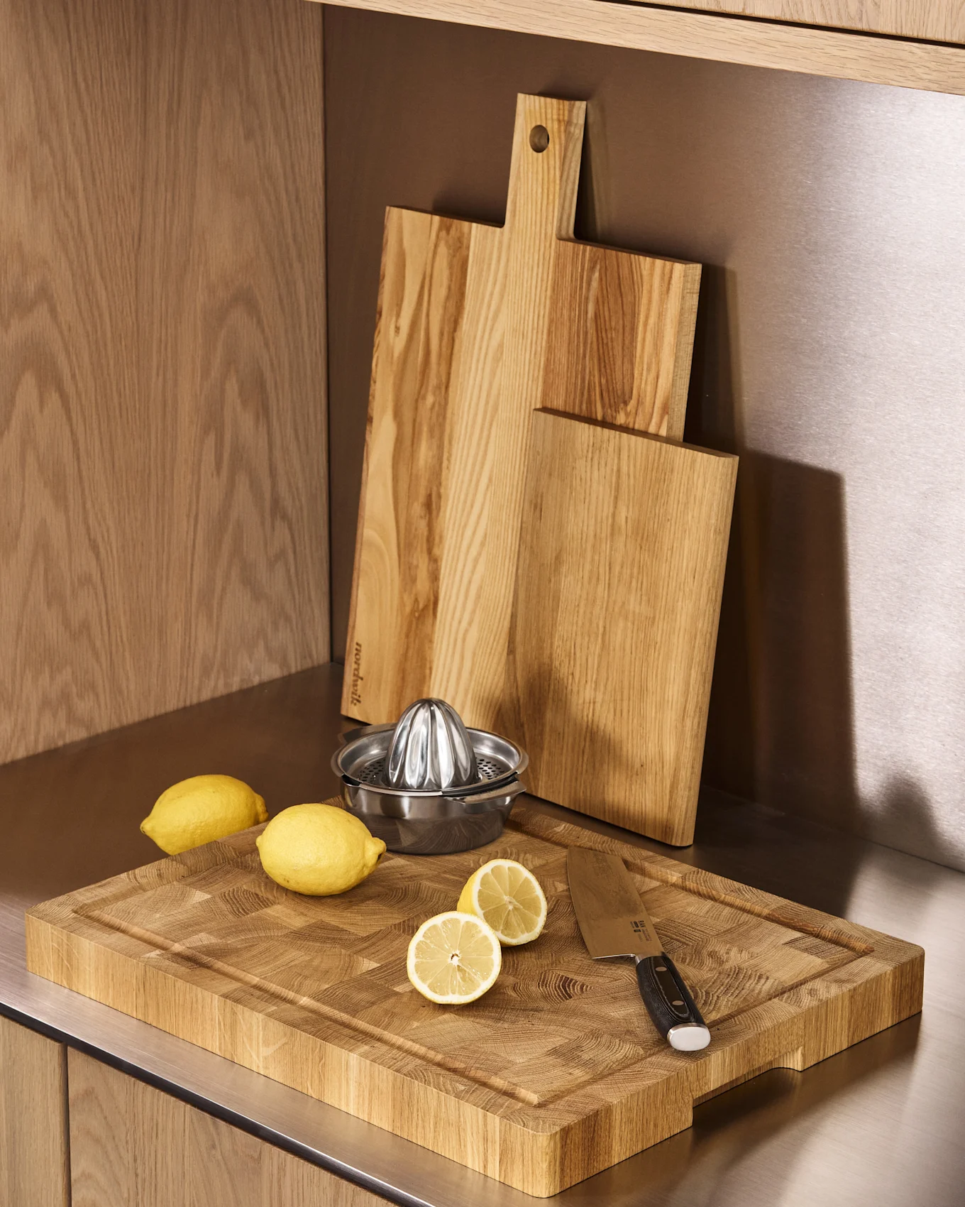 Køkkenbord med tre træskærebrætter, en metalcitronpresser, hele og halverede citroner og en kniv.