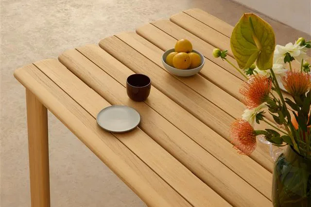 Lyst trælamelbord med en skål citroner, mørkt krus, lille tallerken og en vase med orange og hvide blomster.