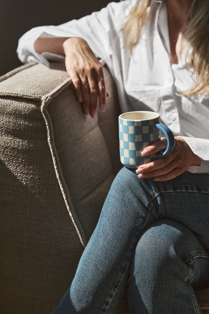 Tern og striber er en af de store trends i efterårets indretningstrends 2024. Her kan du se en kvinde i en lænestol der holder en blåternet kop fra Byon.