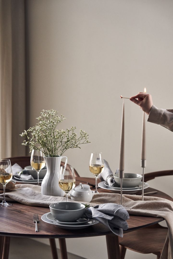 Her kan du se en elegant borddækningside dækket med Swedish Grace tallerkener og skåle i farven Tåge med beige lys fra Ester og Erik.