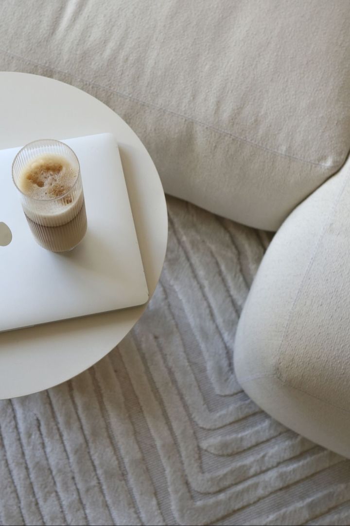 Her ses en perfekt tilberedt latte macchiato i et long drink-glas fra Ferm Livings Ripple-kollektion på et sofabord ved siden af en beigefarvet sofa i @ellesklingens hjem.