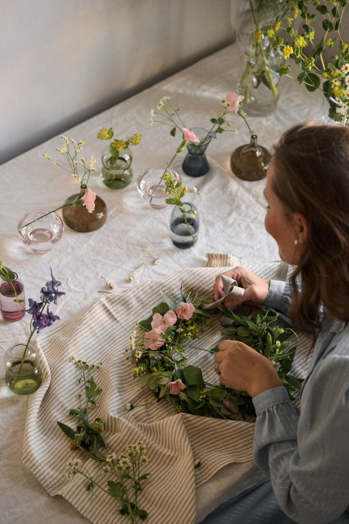 Her ses en blomsterkrans der er ved at blive flettet med flere forskellige blomster, der er blomster i Midsommer mini vaserne fra Orrefors.