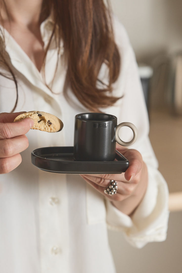 Her ser du en kvinde, der holder Niki-espressokoppen fra Byon i den ene hånd og en biscotti i den anden.