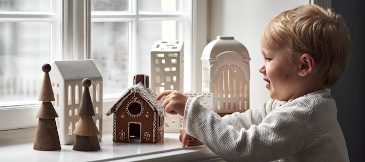 Sådan pynter du op med traditionelt skandinavisk julepynt - her ser du en ung dreng, der spiser et peberkagehus i vindueskarmen omgivet af andre lysestager i peberkagehusstil.