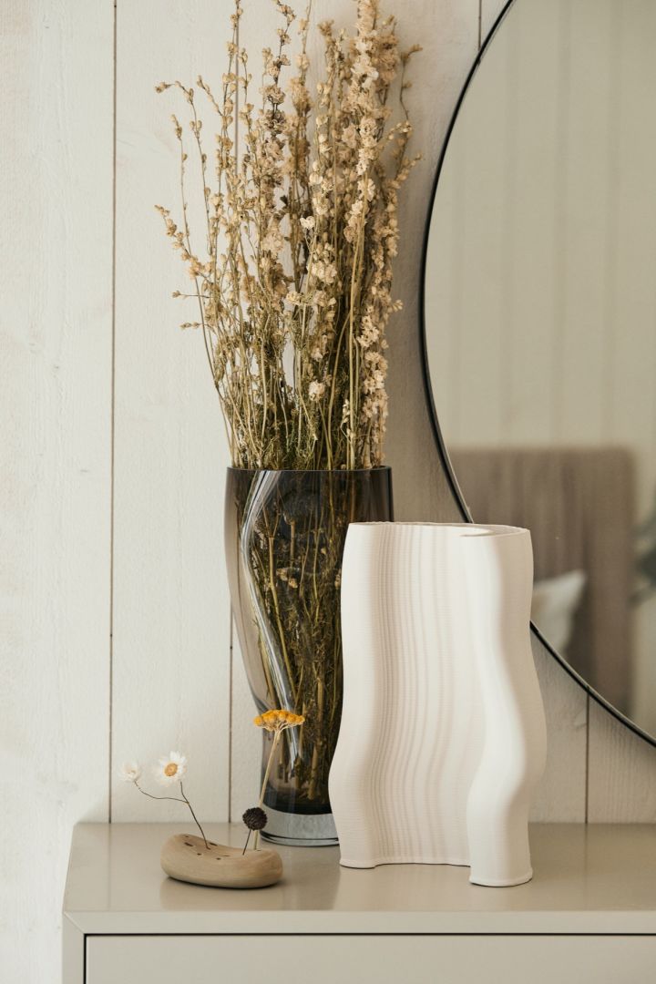 Den 3D printede Moire vase fra Ferm Living står på en kommode sammen med en vase fuld af tørrede blomster. Vasen viser taktilt materiale og struktur hvilket er en af de store trends i efterårets indretningstrends 2024.