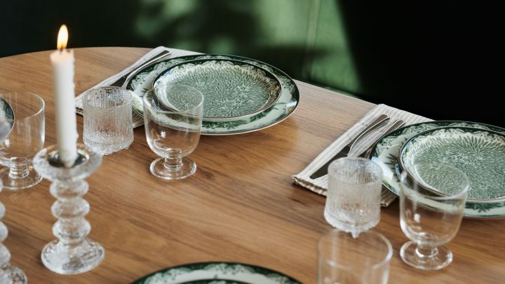 Design klassiske Ostindieblomster i grønt i en restaurantdækning med grove lysestager i glas.