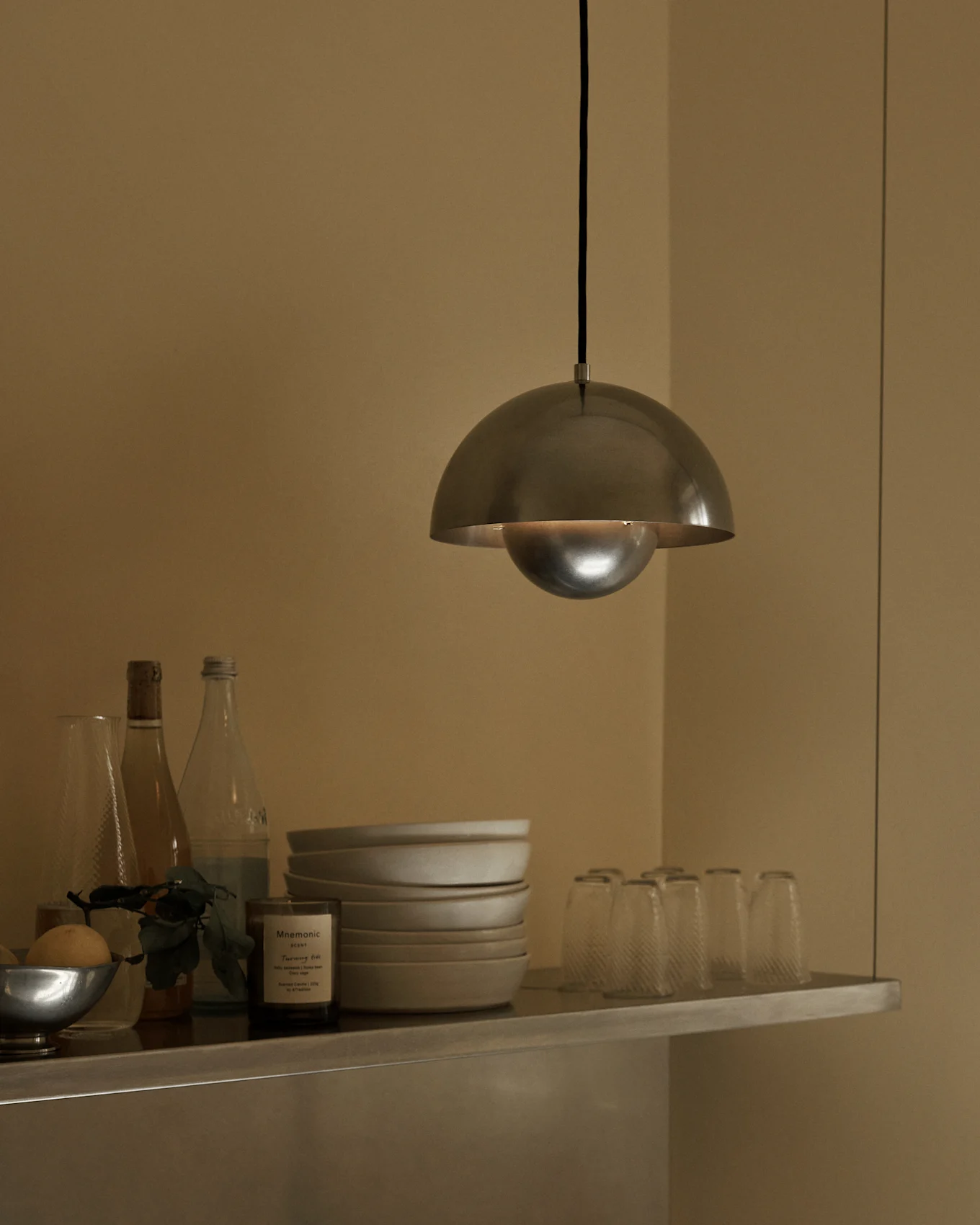 En børstet metal kuppelpendel hænger over en hylde med skåle, flasker og glas.