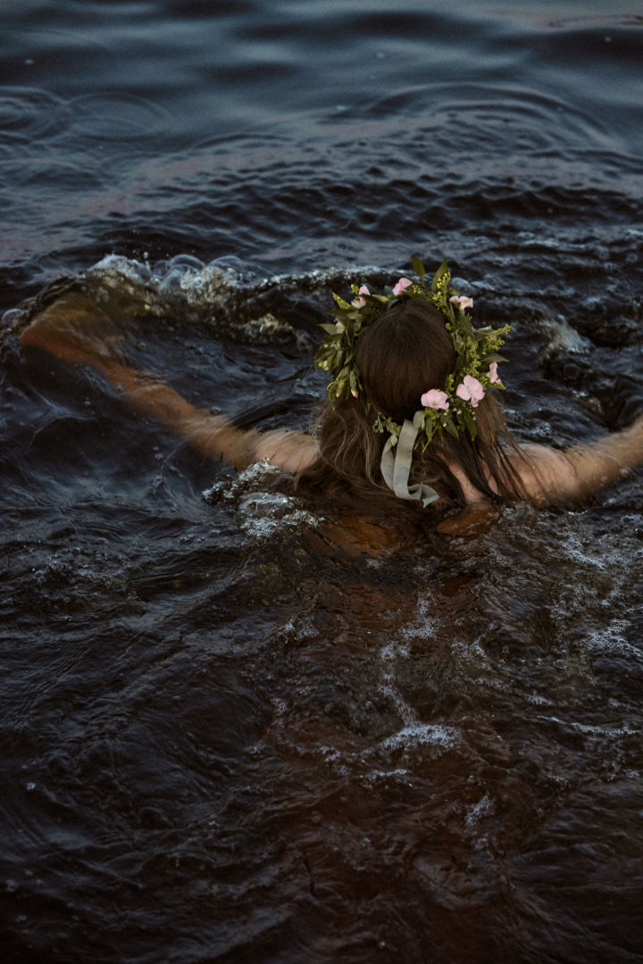 Her ses en kvinde tage en dukkert i e sø med hendes midsommer krans på.