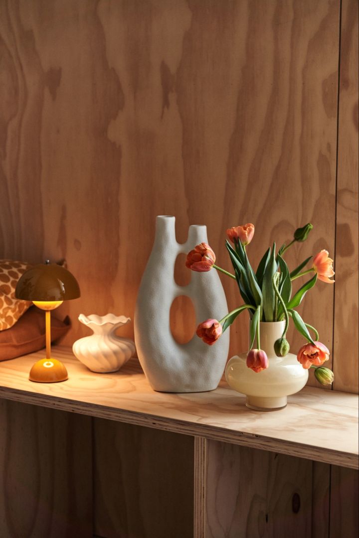 Her står en portabel lampe, skulptur og en vase med friske blomster for at skabe visuel interesse i et rum. 