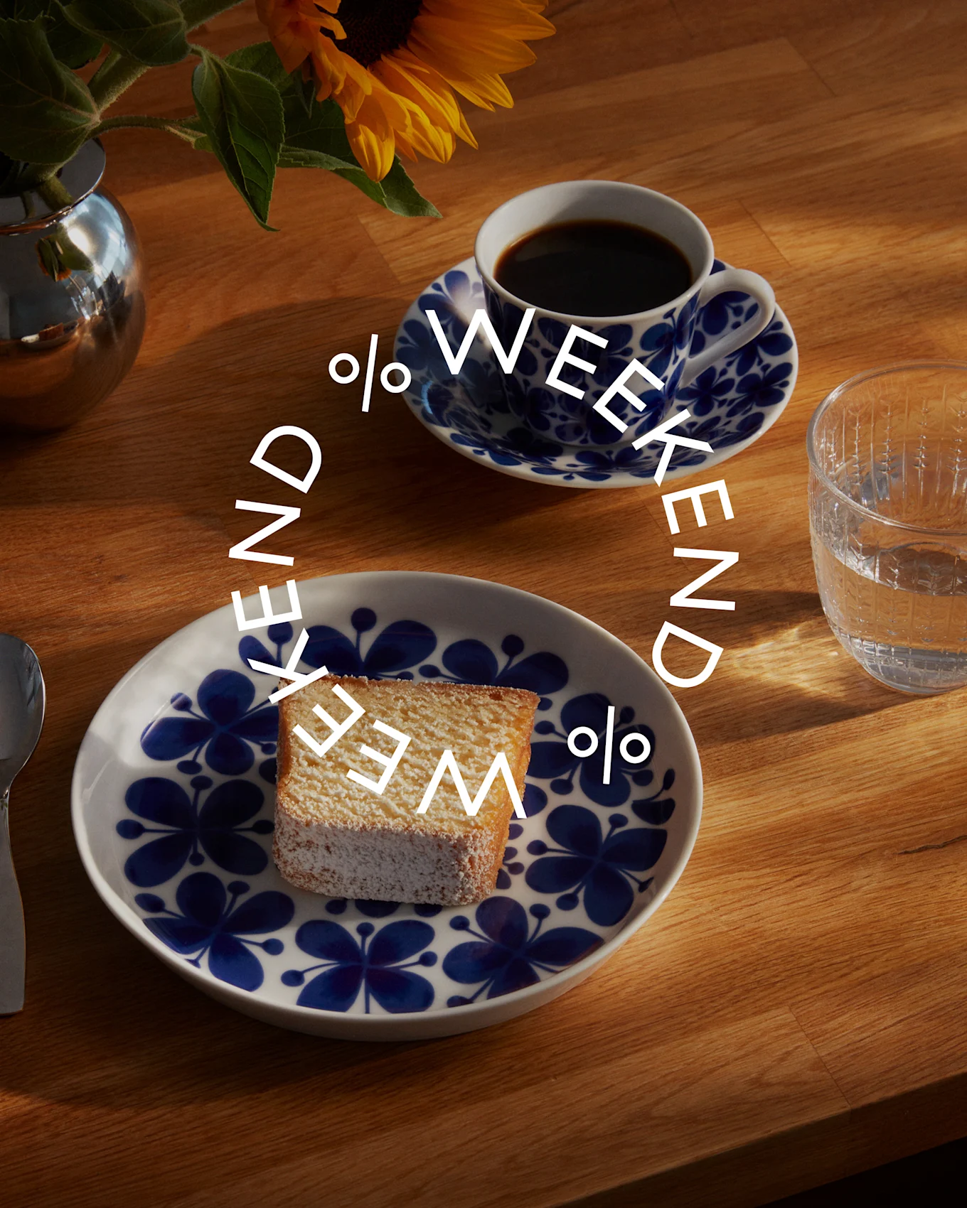 Ovenfra billede af en kaffekop, kageskive på en tallerken og et glas vand på et træbord, med teksten 'WEEKEND' i en cirkel.