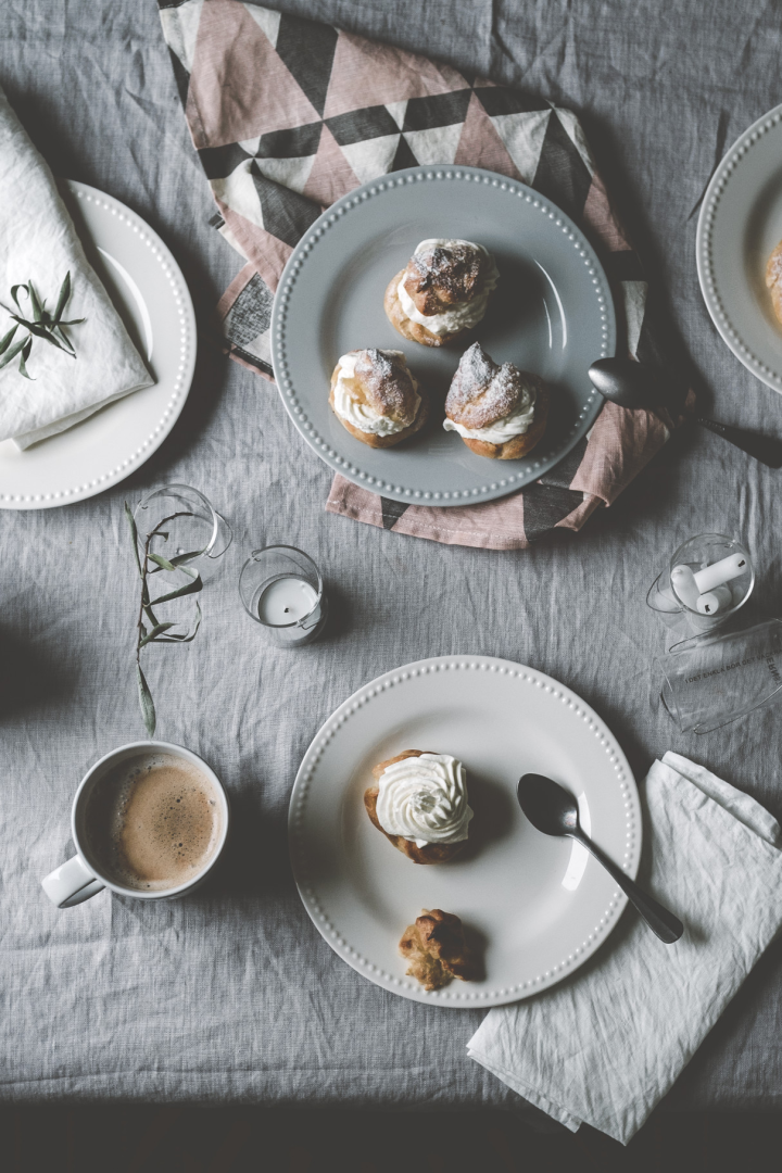 Her kan du se @kohlundkimchis Semlor stå på et bord på forskelligt farvede tallerkener fra Dots-kollektionen fra Scandi Living, ledsaget af en kop kaffe.