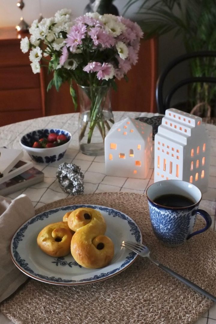 Her ses et bord med friske blomster og julepynt i form af Urbania-lysestager fra Kähler og svenske lussekatter på en Ostindia-tallerken fra Rörstrand hjemme hos @_mariano_rivera_4242.